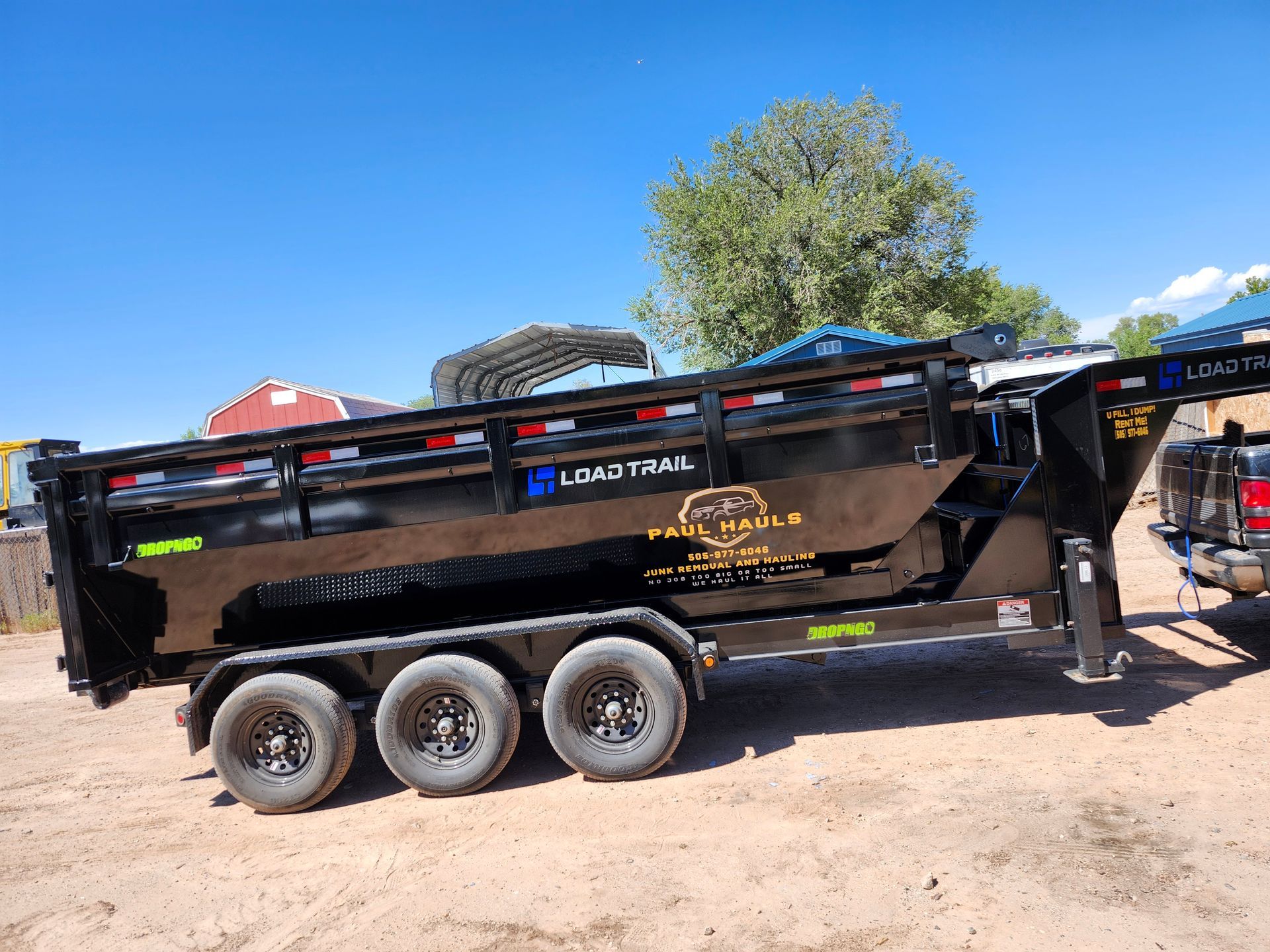 A dump trailer is parked in a dirt lot next to a truck.