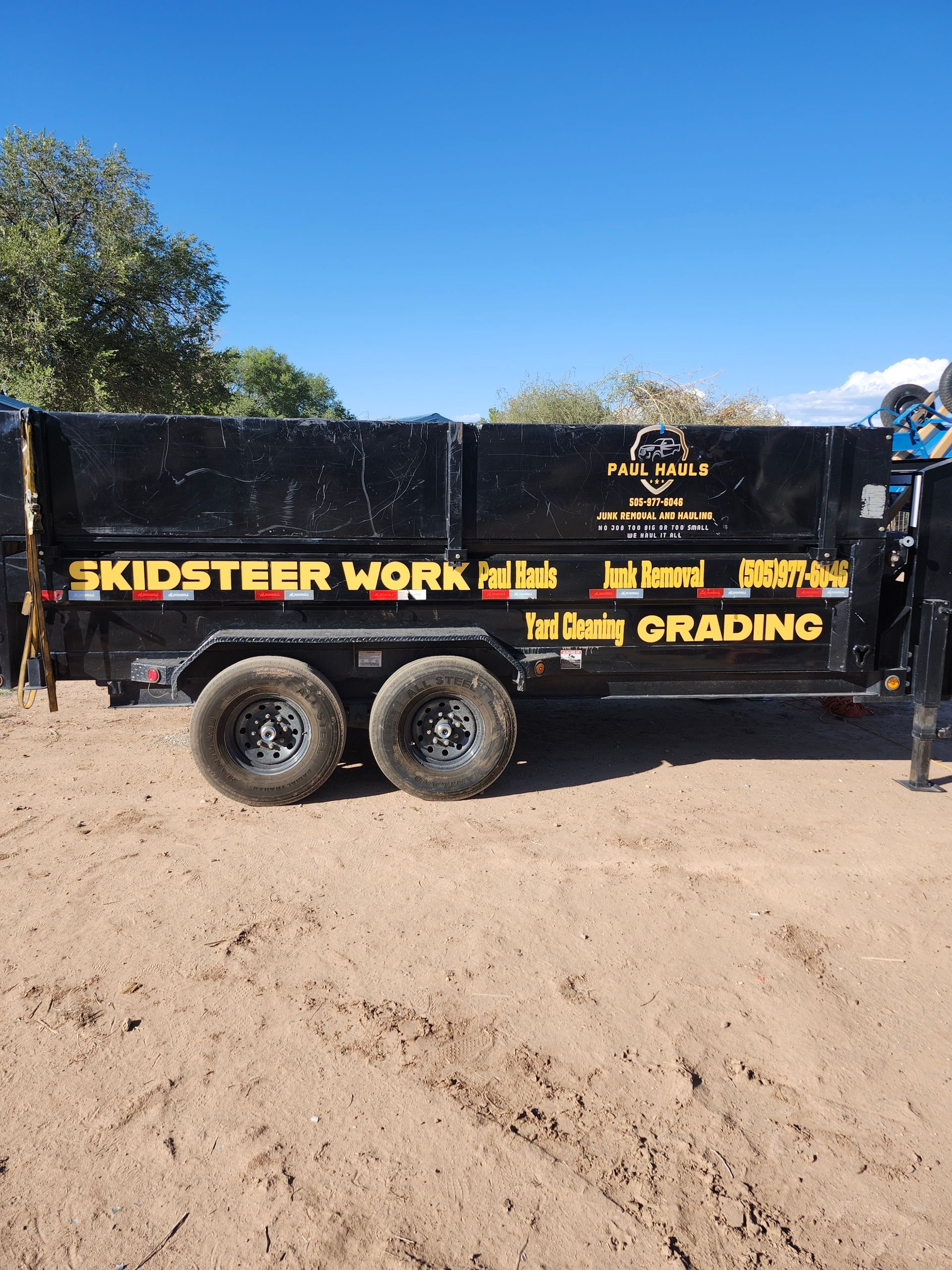A skidsteer work dumpster is parked in the dirt