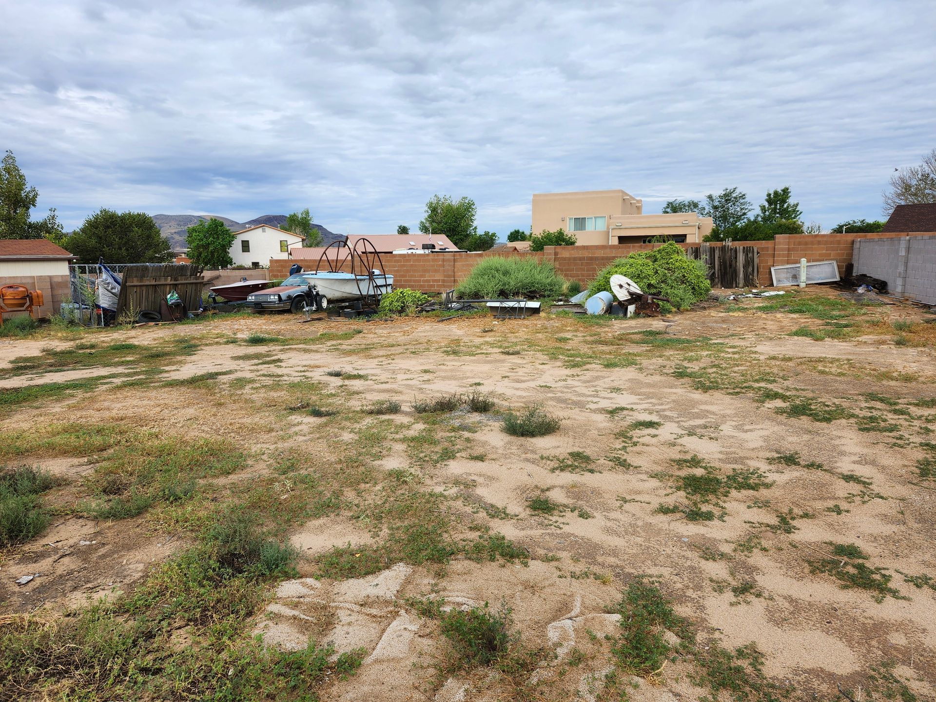 A large dirt field with a fence in the background and a house in the background.