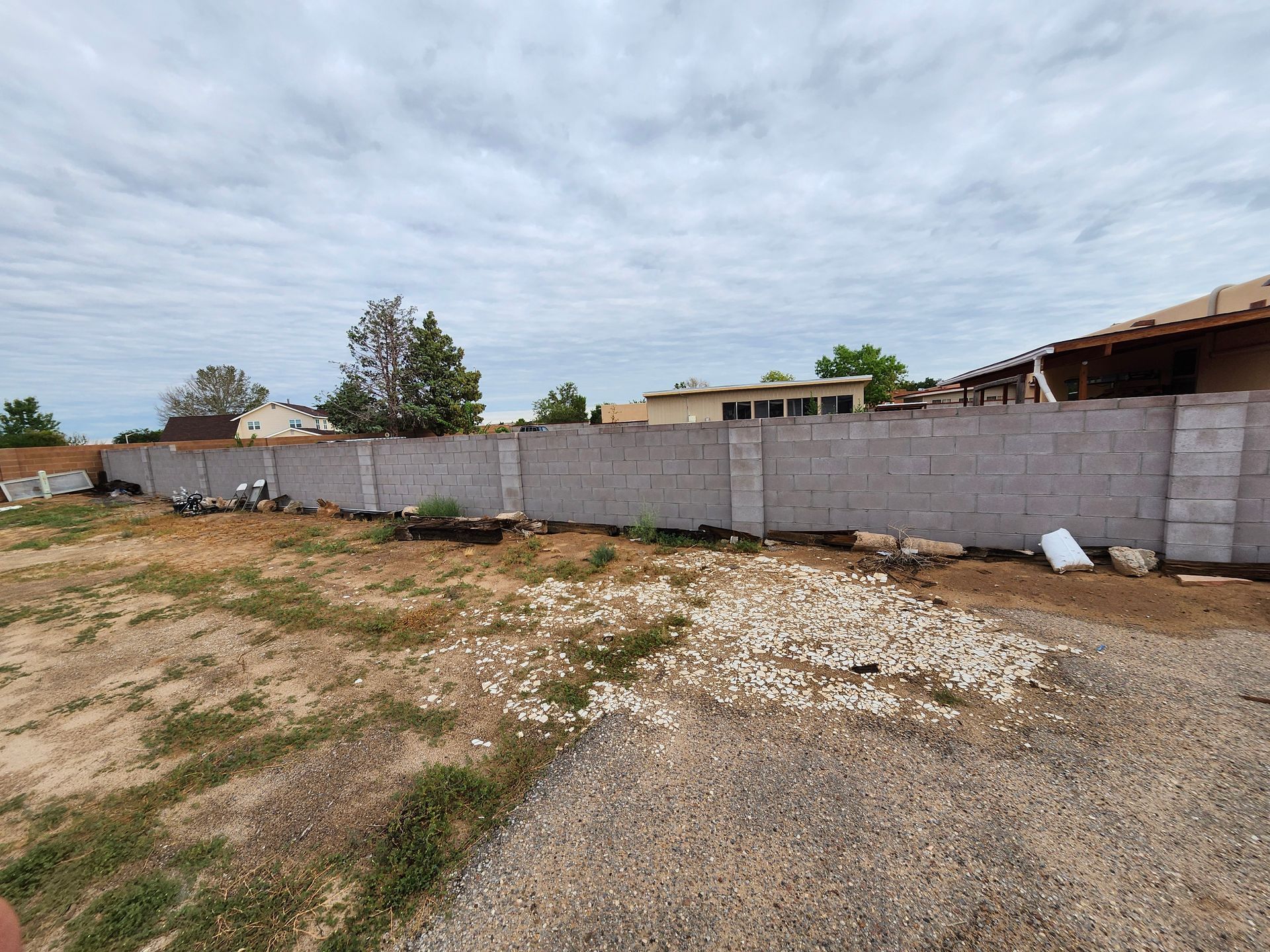 A brick fence surrounds a dirt field with a house in the background.