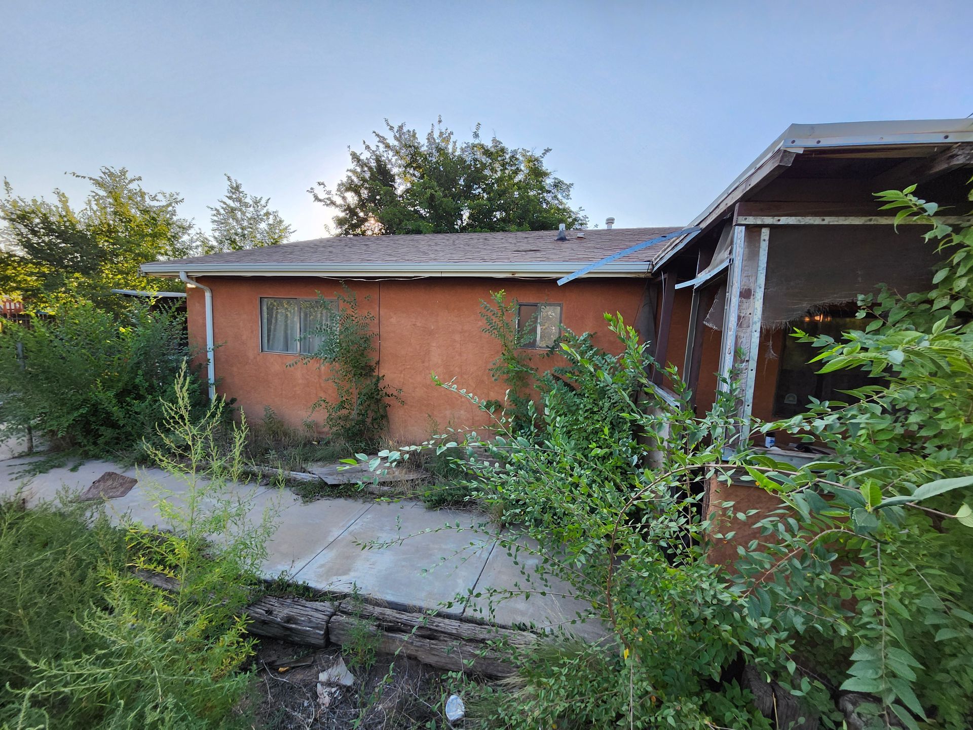 A small house with a porch is surrounded by trees and bushes.