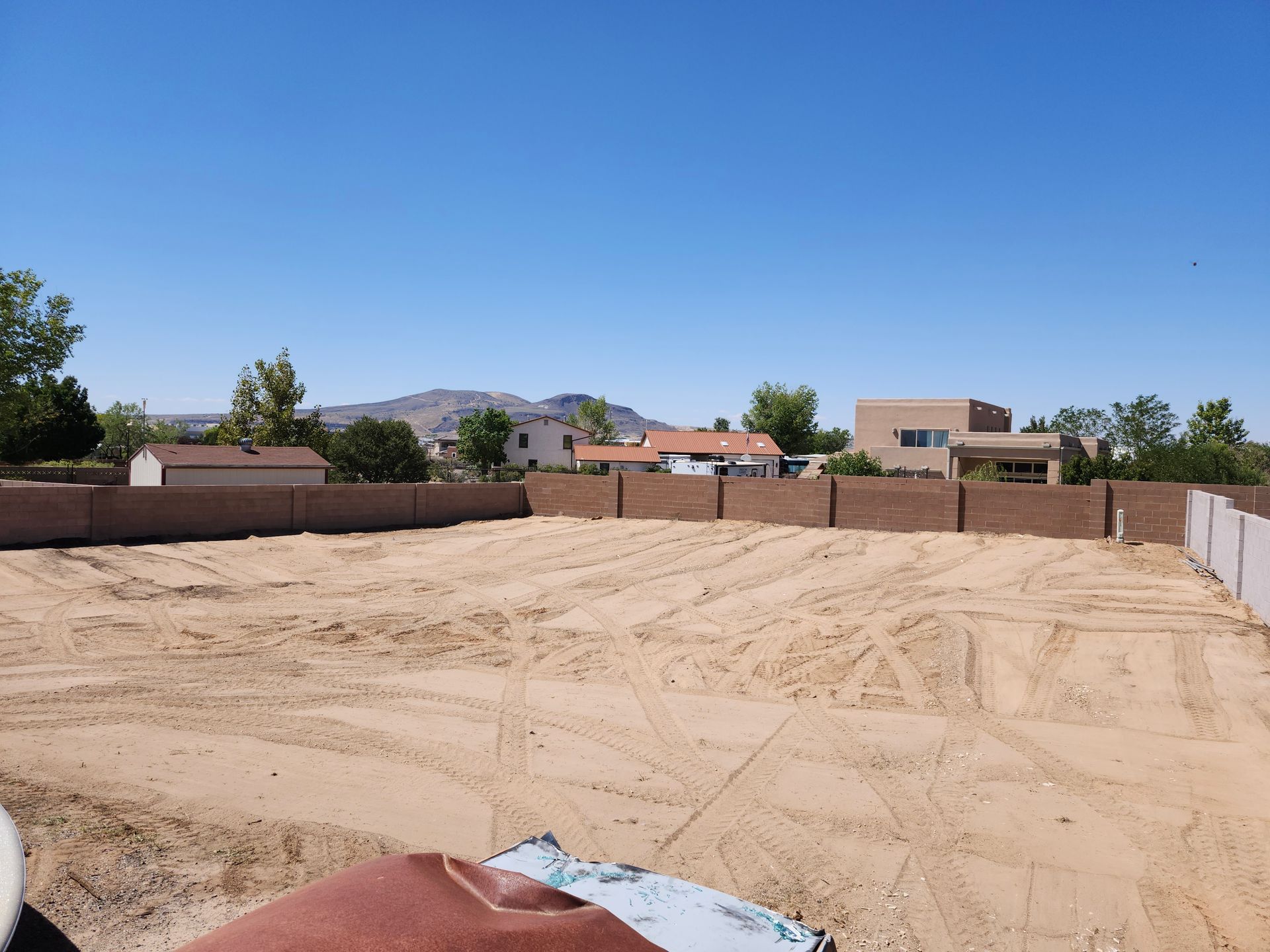 A large dirt field with a fence and houses in the background
