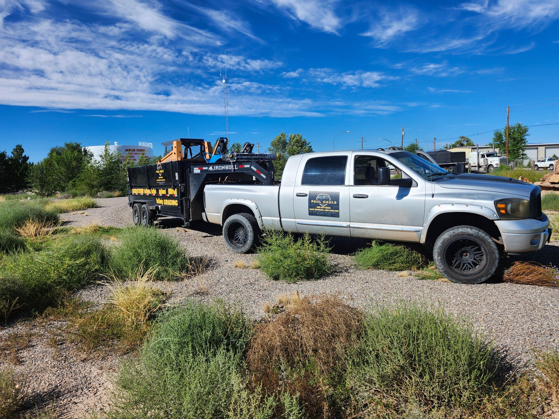 A truck with a trailer attached to it is parked in a dirt field.