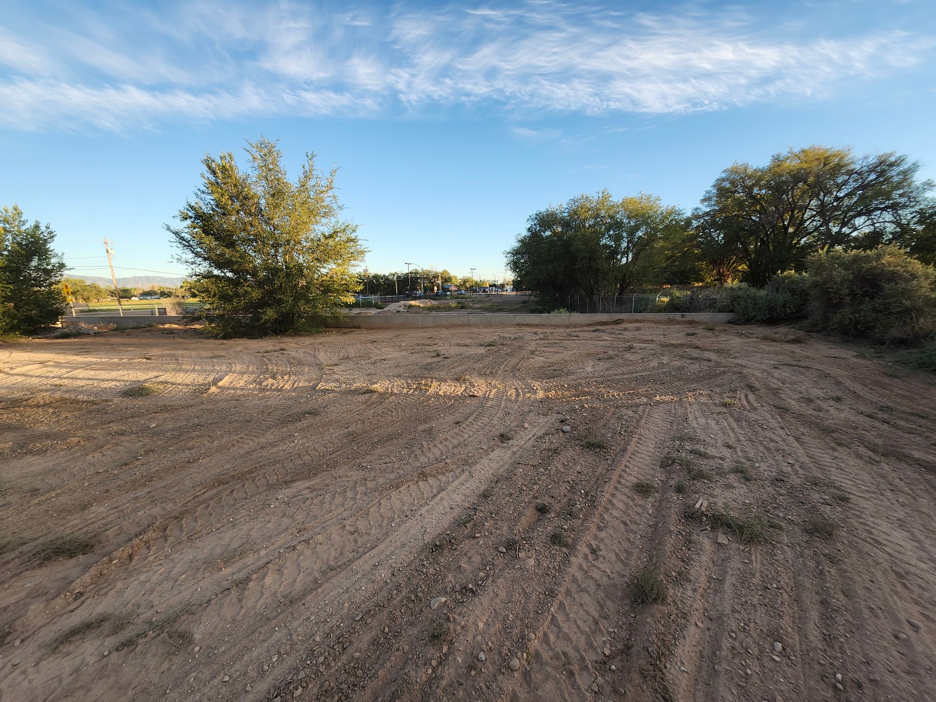 A dirt field with trees in the background and a blue sky