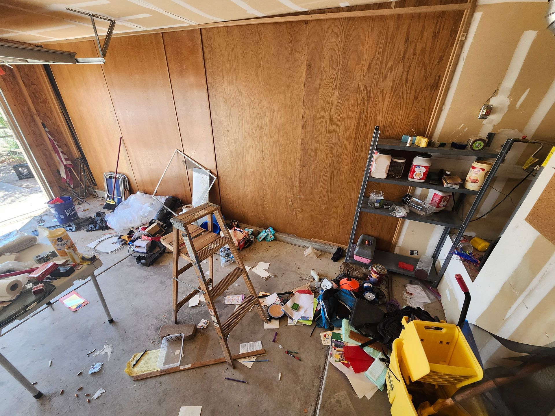 A messy garage with a ladder and a mop.
