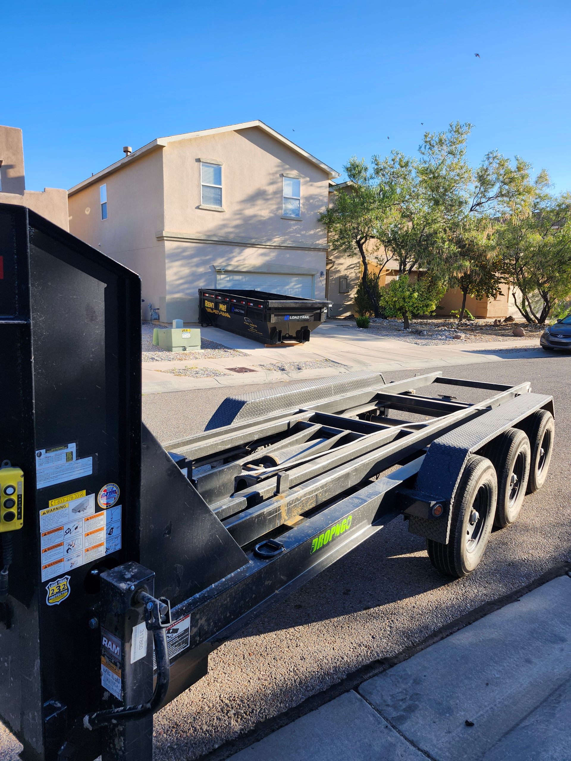 A dumpster trailer is parked on the side of the road in front of a house.