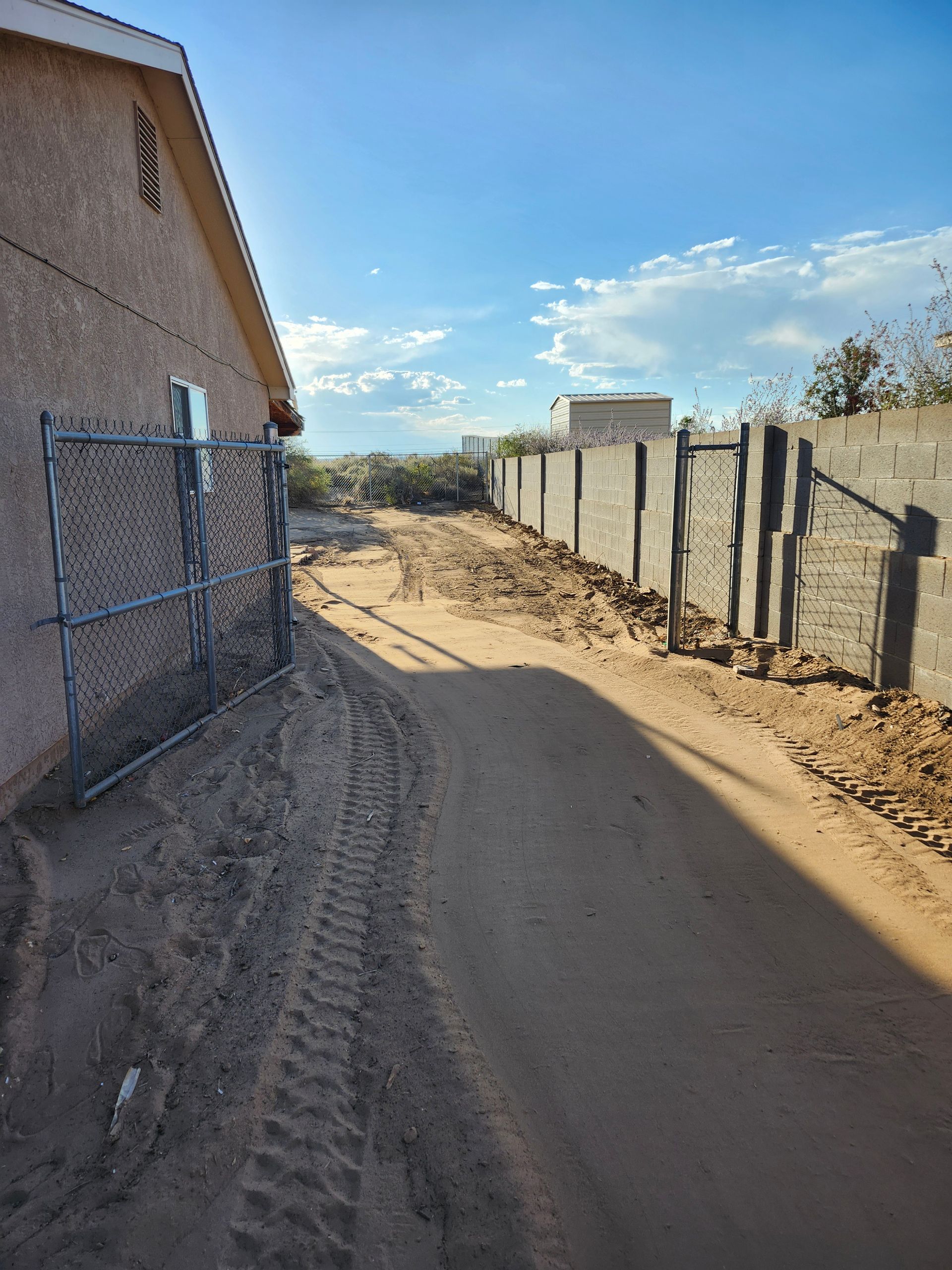 A dirt road leading to a house with a chain link fence.