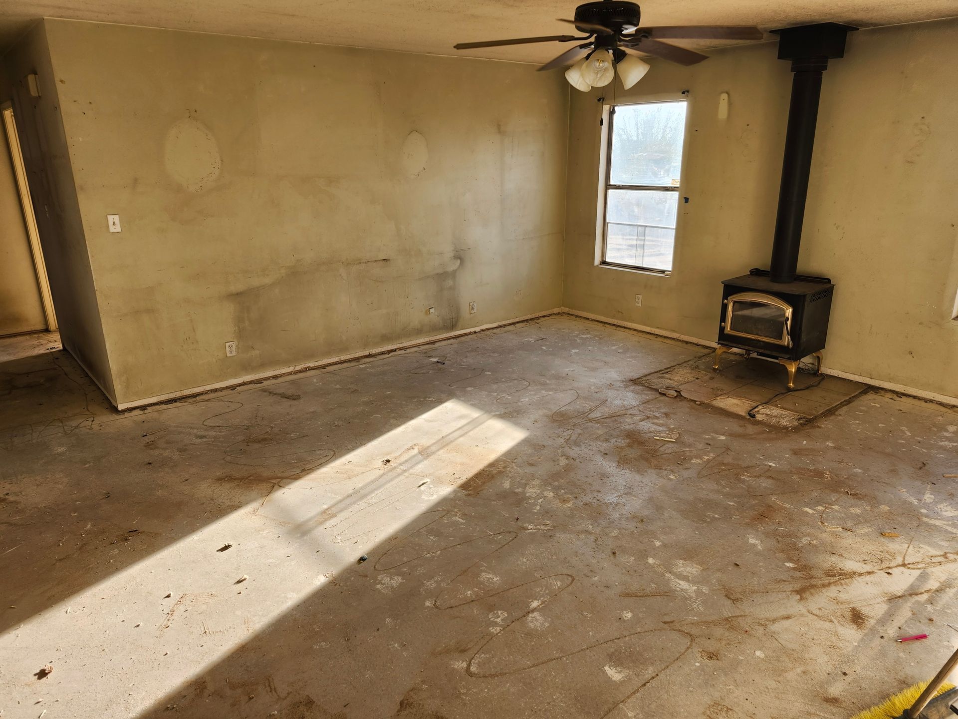 An empty living room with a wood stove and a ceiling fan.