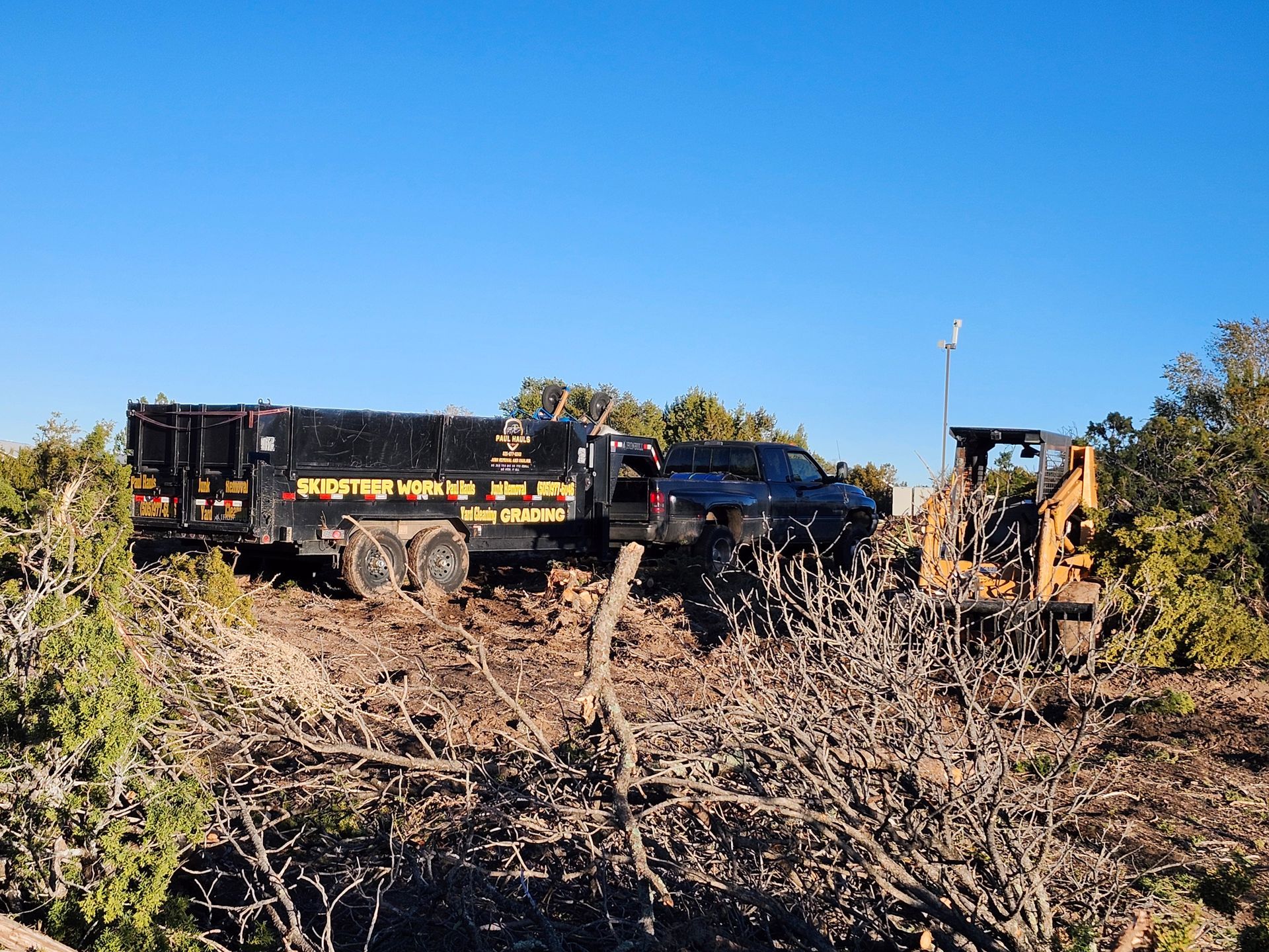 A truck with a trailer attached to it is driving down a dirt road next to a bulldozer.