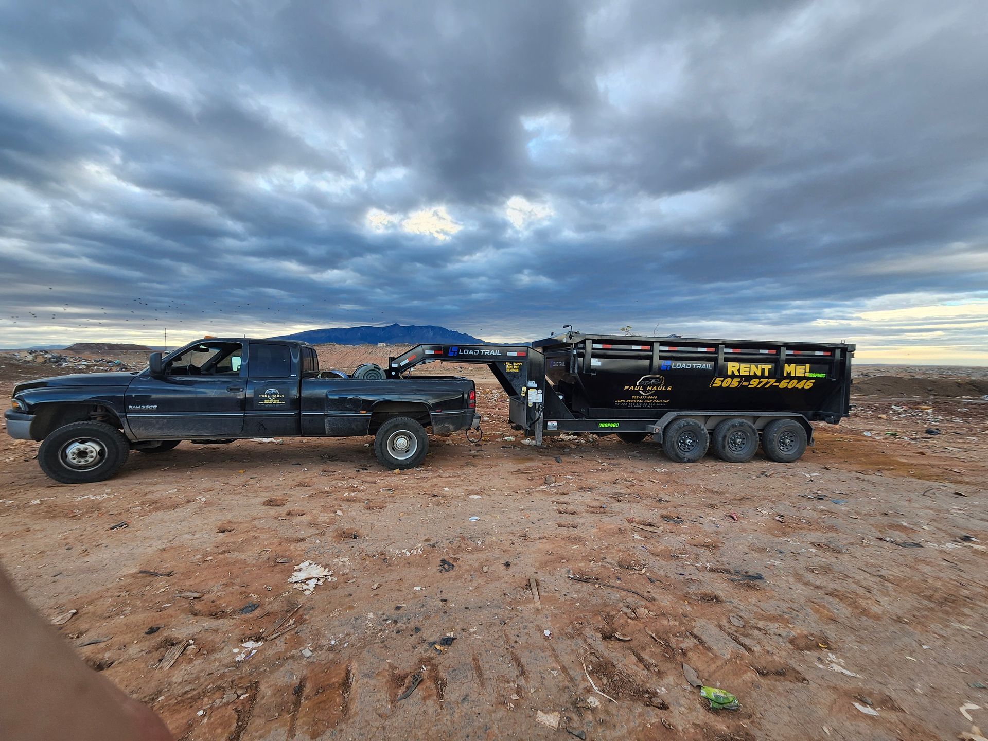 A truck is towing a dumpster in the desert.