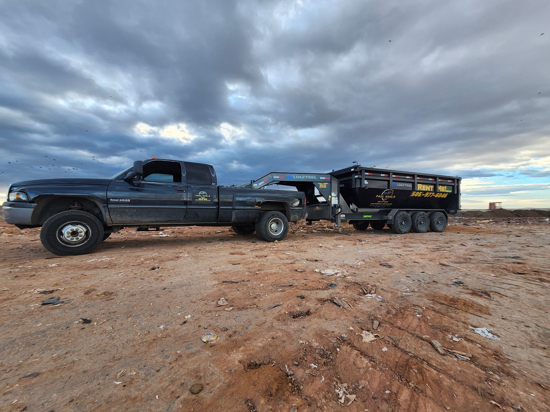 A black truck with a trailer attached to it is parked in a dirt field.