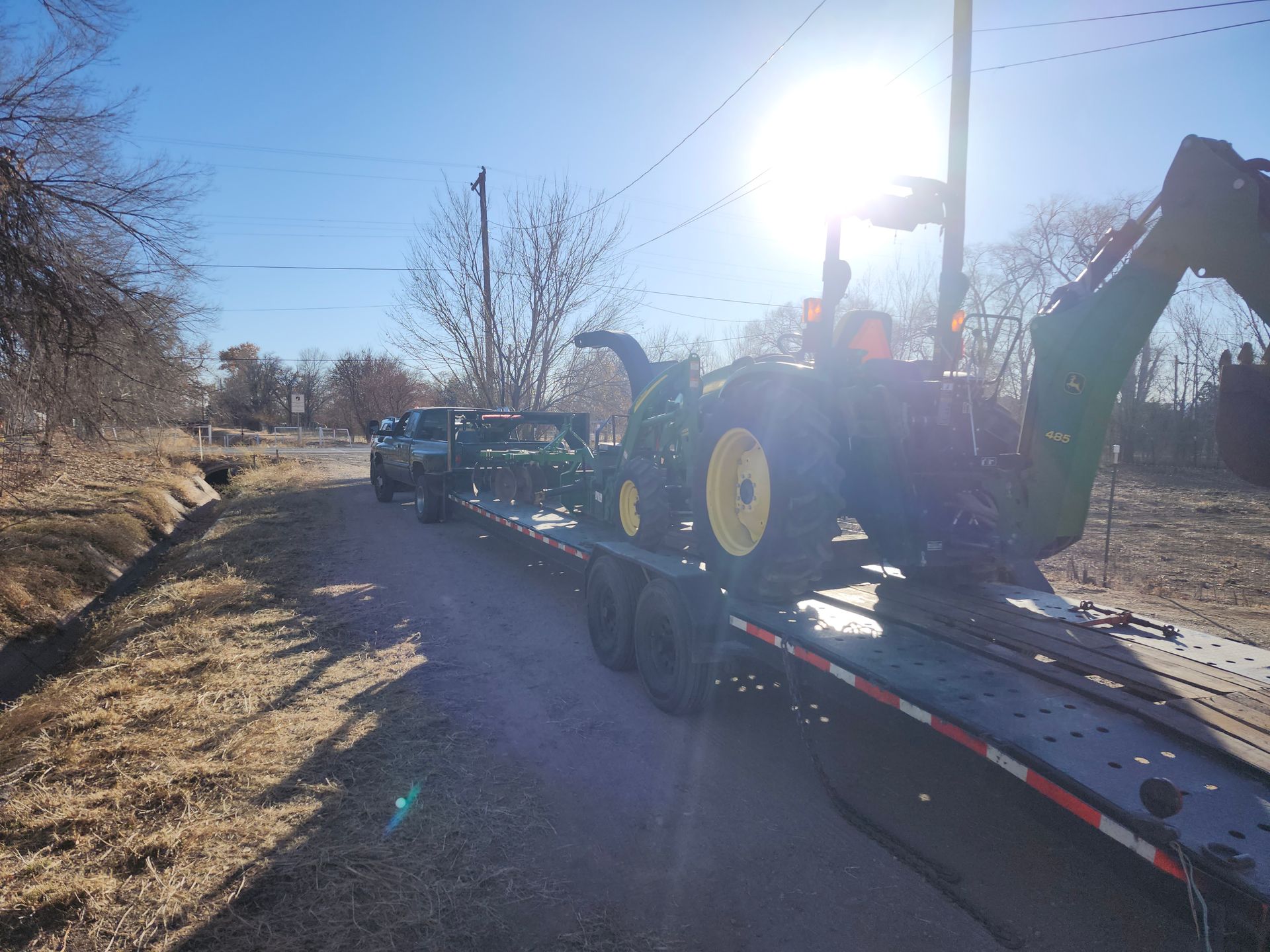 A tractor is being towed on a trailer down a dirt road.