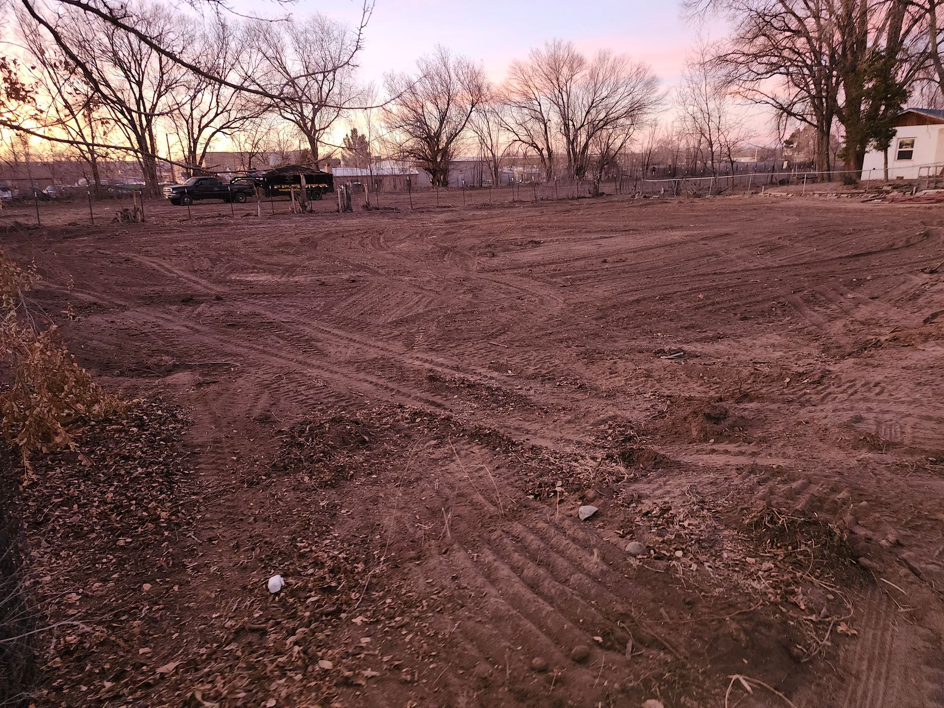 A dirt field with trees in the background and a sunset in the background.
