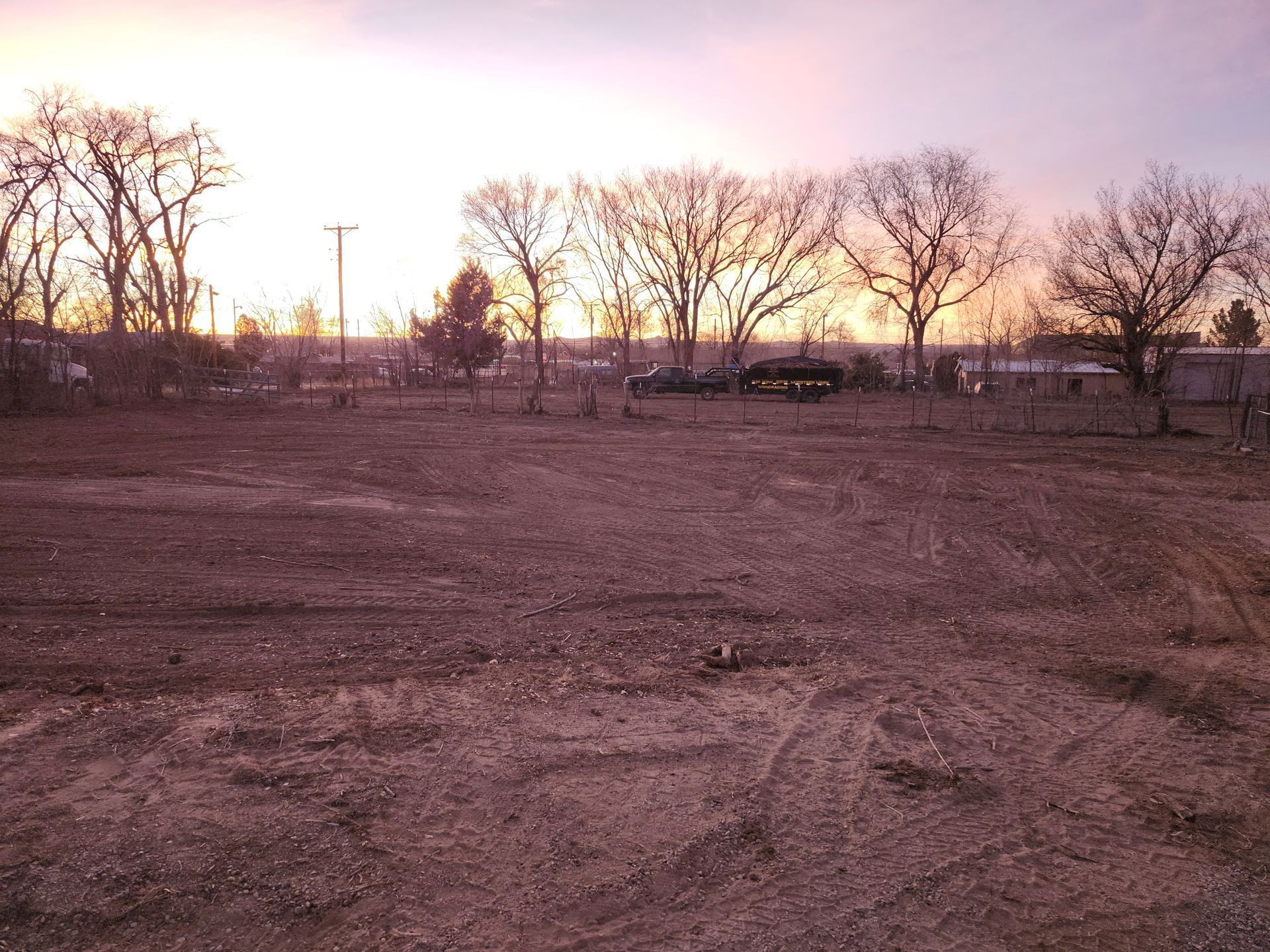 A sunset over a dirt field with trees in the background
