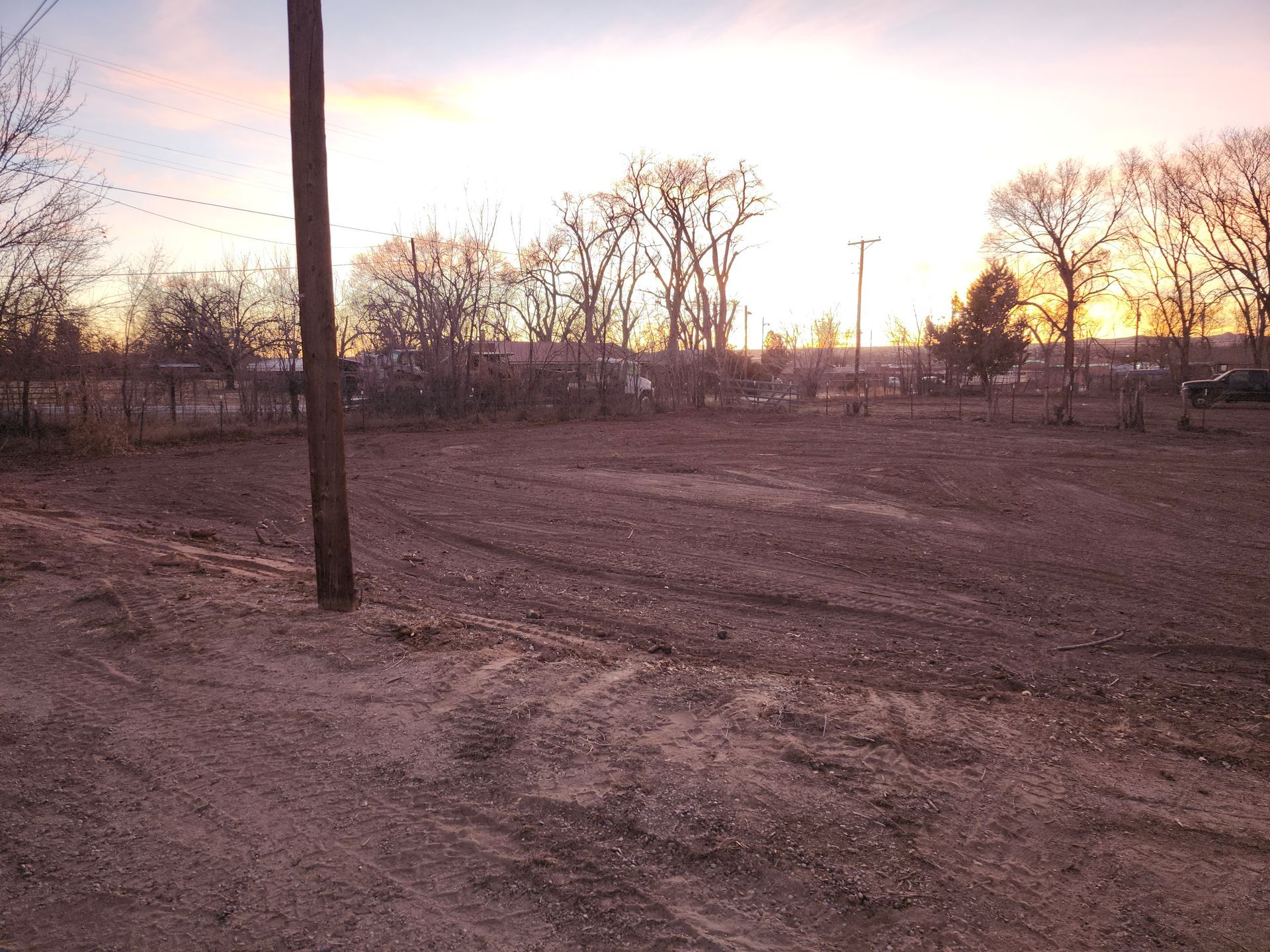 A sunset over a dirt field with trees in the background