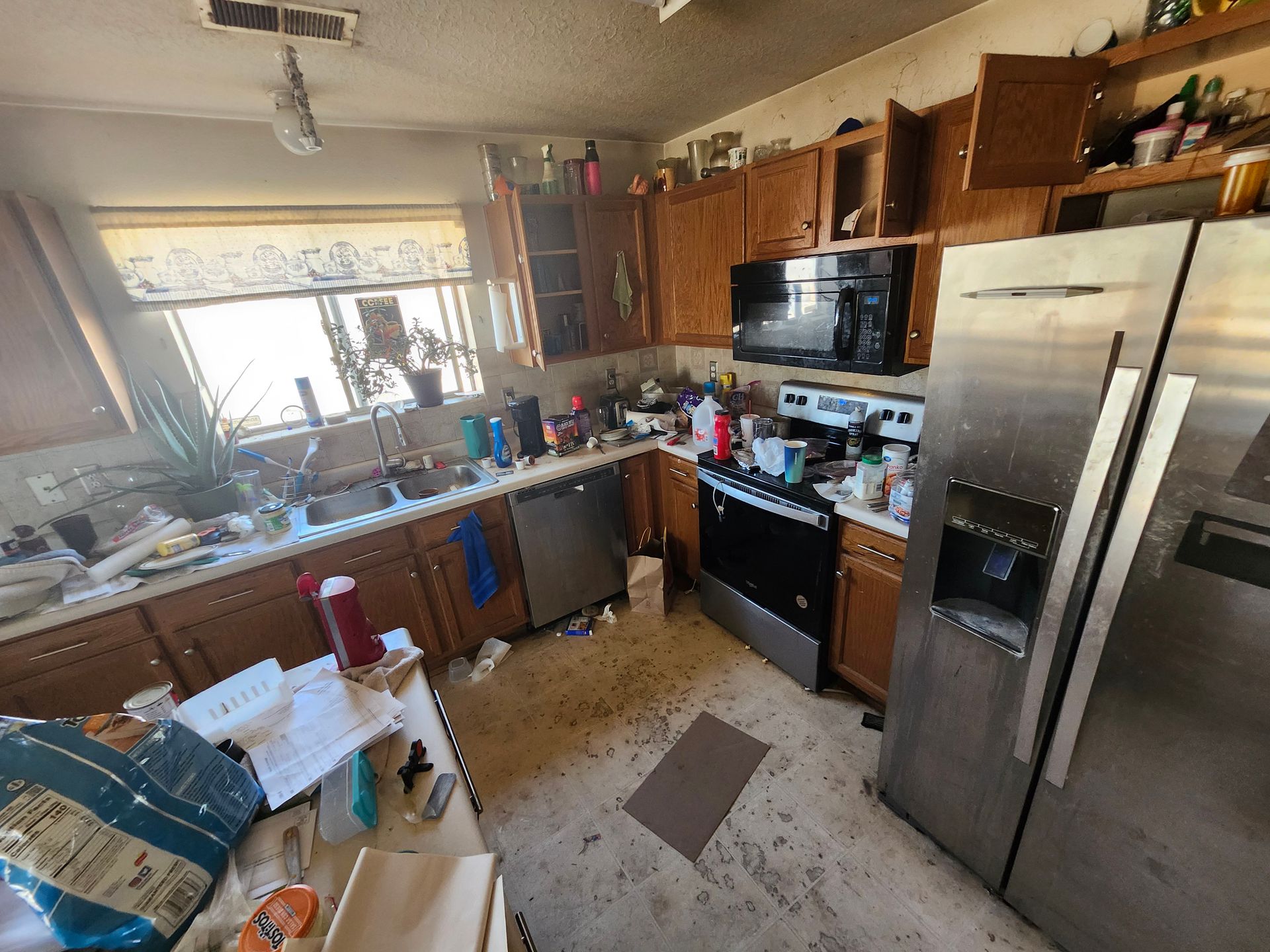 Cluttered kitchen with stainless steel appliances, brown cabinets, and items on counters.
