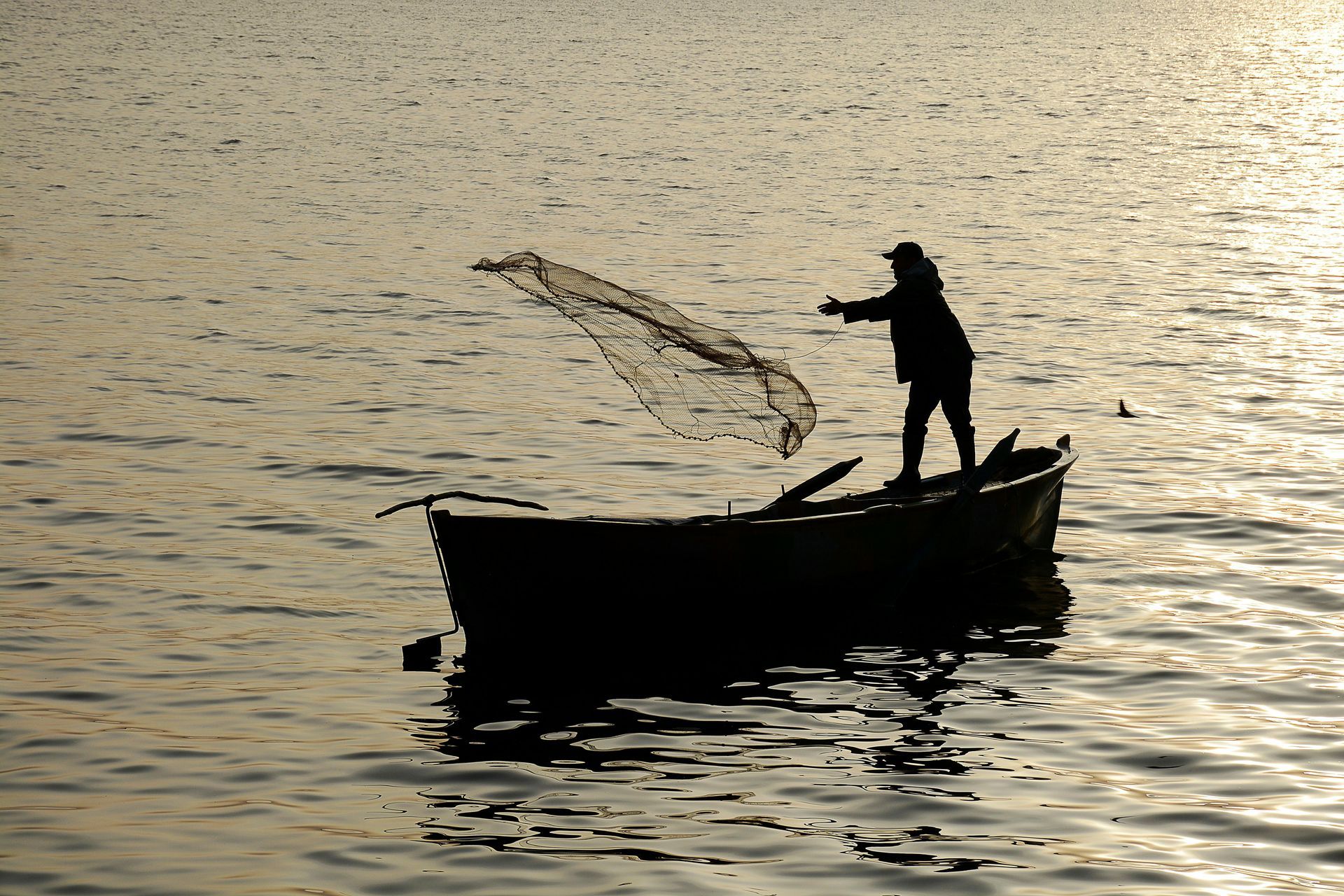 A man in a boat is throwing a net into the water