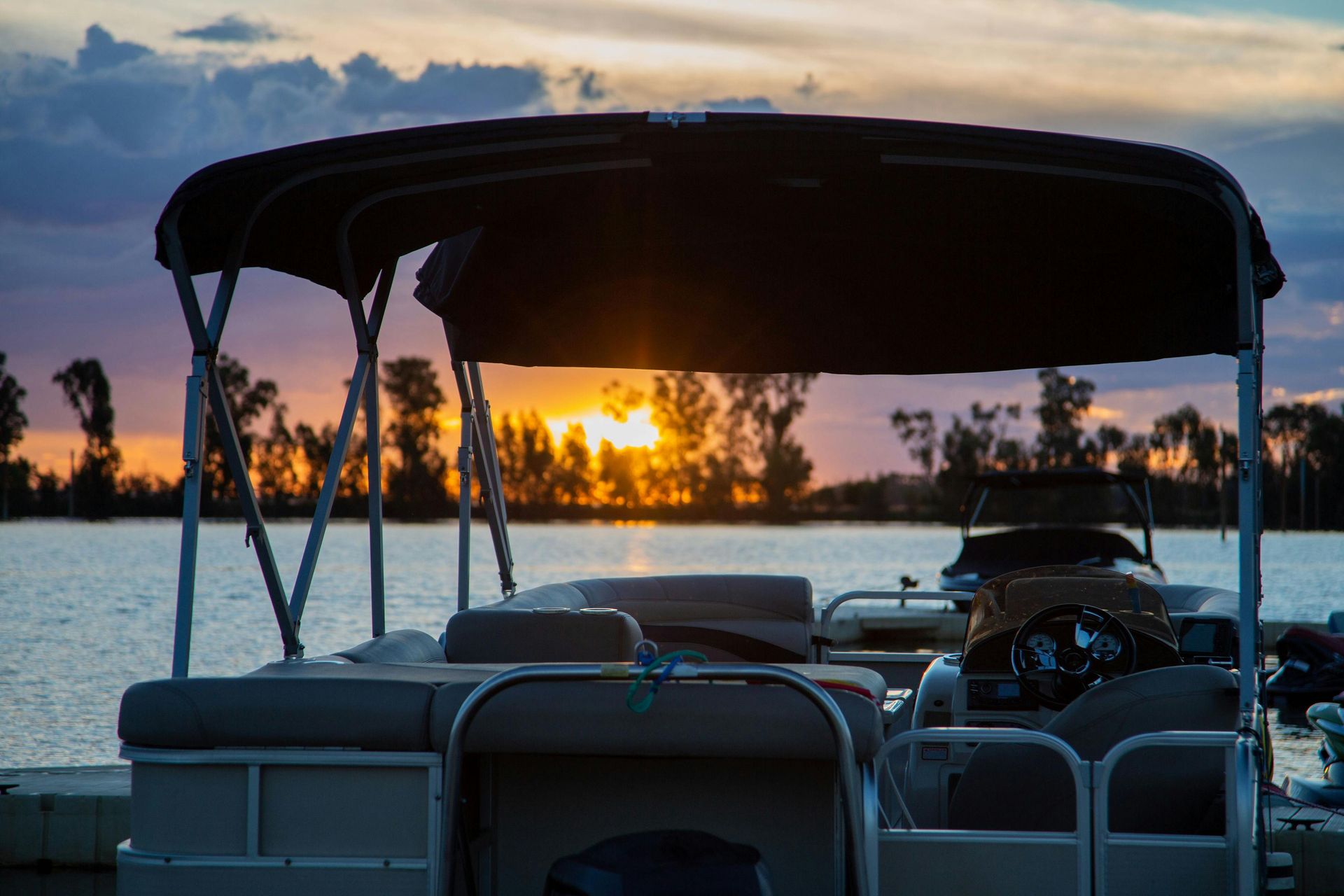 A pontoon boat is docked on a lake at sunset.