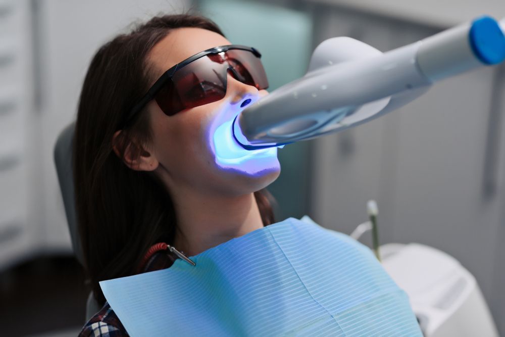 A woman is getting her teeth whitened in a dental office
