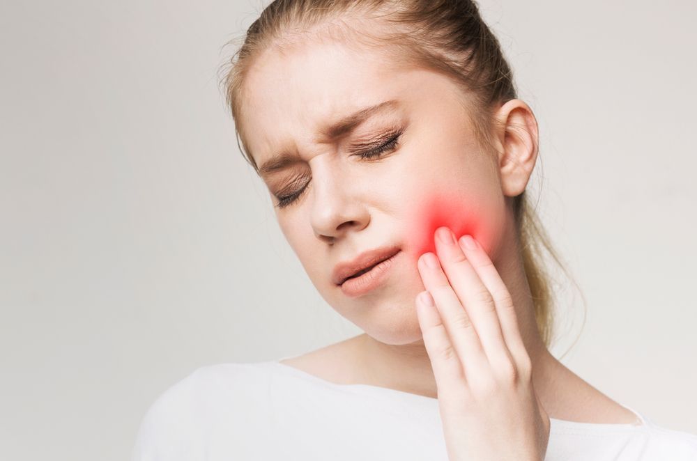 A Woman is Holding Her Face in Pain Because of a Toothache — Cairns Precision Dental Group In Woree, QLD