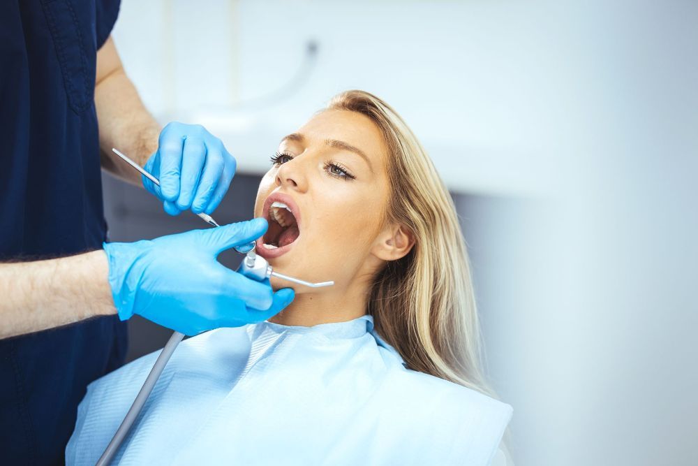 A Woman is Sitting in Front of a Machine With a Caution Sign Behind Her — Cairns Precision Dental Group In Woree, QLD