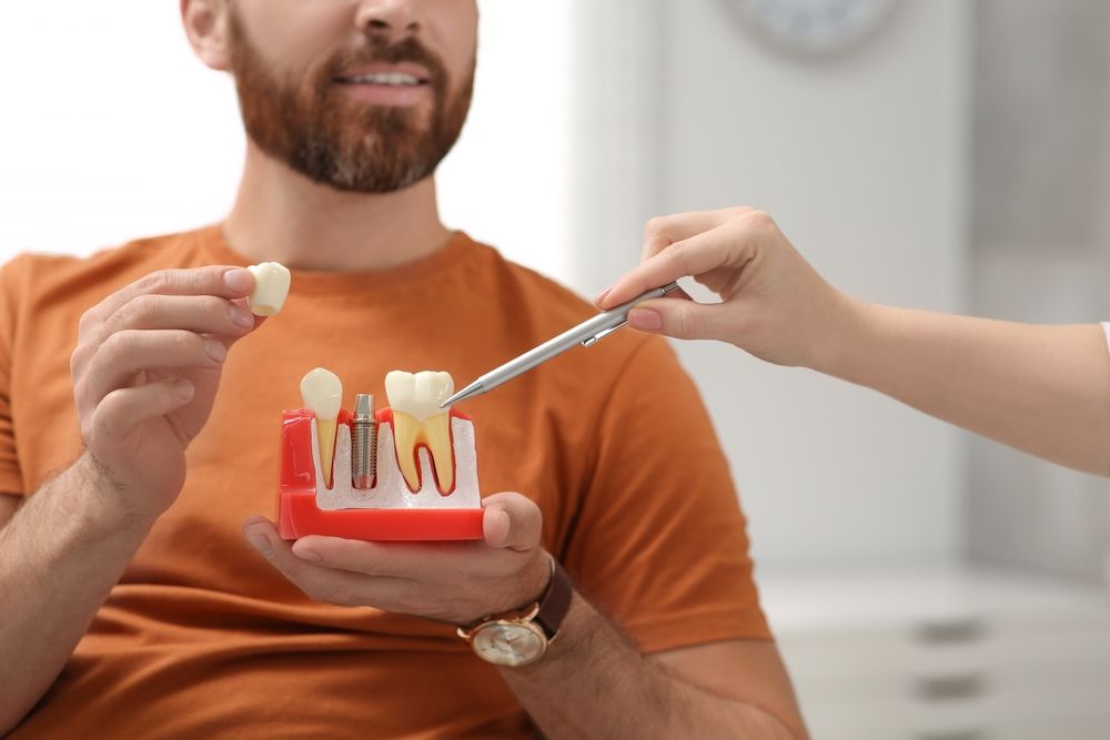 A Man is Holding a Tooth Color Chart in Front of His Mouth — Cairns Precision Dental Group In Woree, QLD