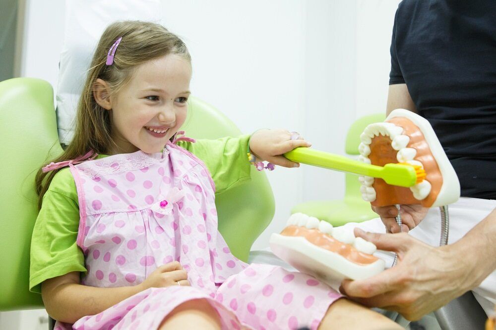 A Little Girl is Sitting in a Dental Chair Brushing Her Teeth — Cairns Precision Dental Group In Woree, QLD