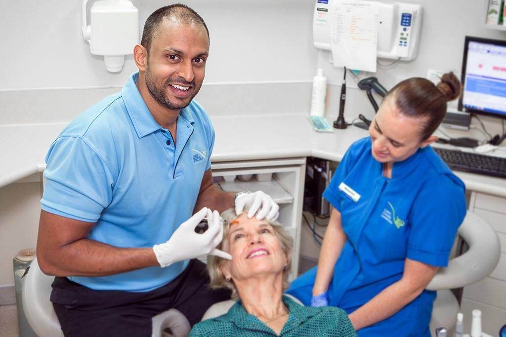 Dentist and assistant treating a smiling patient in a clinic.