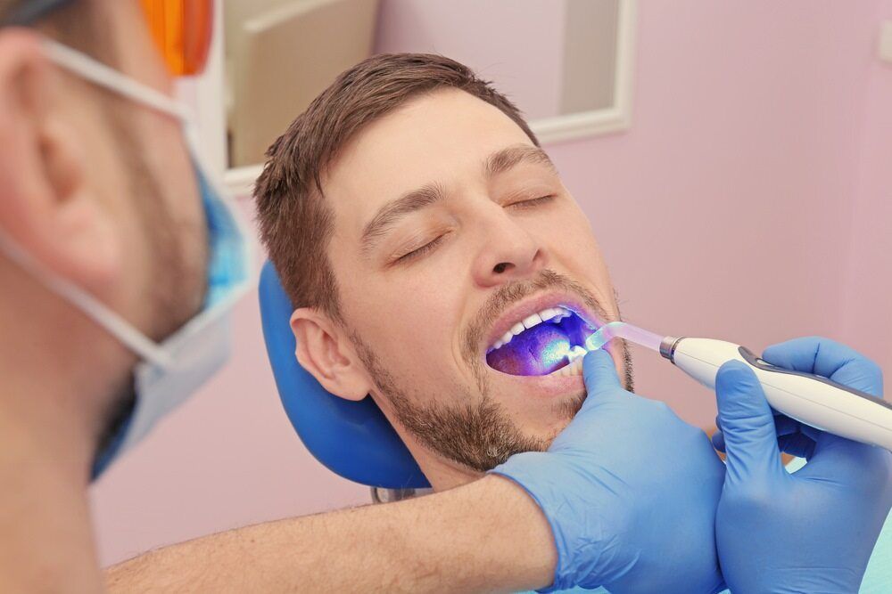 A Man is Sitting in a Dental Chair Getting His Teeth Examined by a Dentist — Cairns Precision Dental Group In Woree, QLD