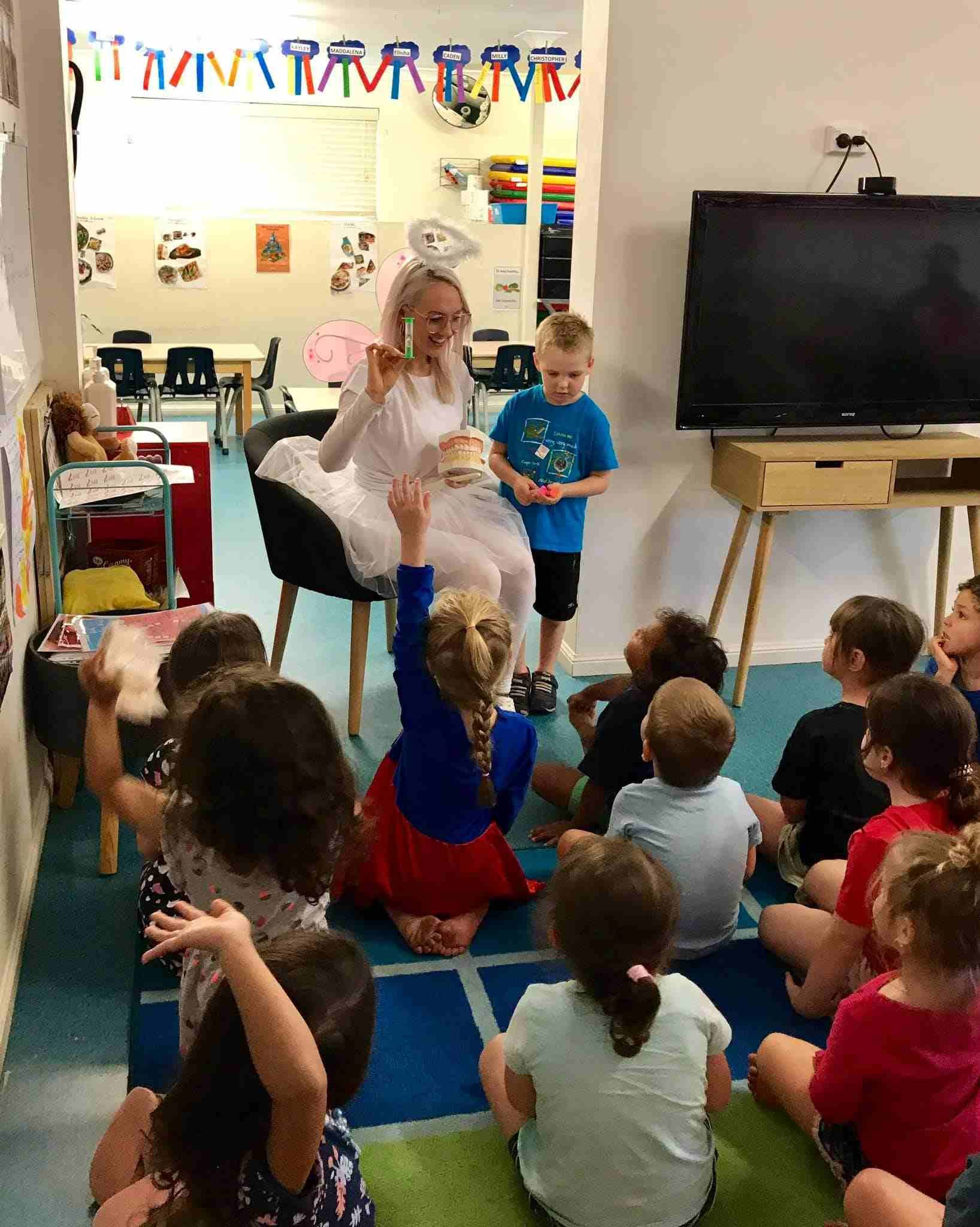 A Group Of Children Are Sitting On The Floor In A Classroom While A Fairy Talks To Them