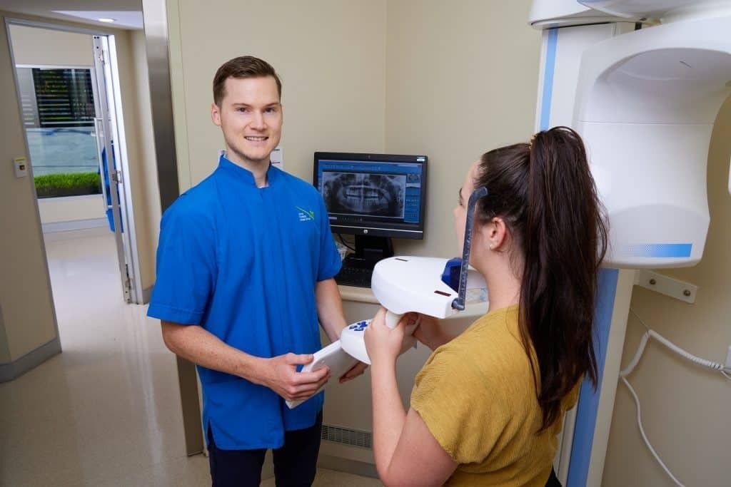 A Woman is Getting an X-ray of Her Teeth by a Dentist — Cairns Precision Dental Group In Woree, QLD