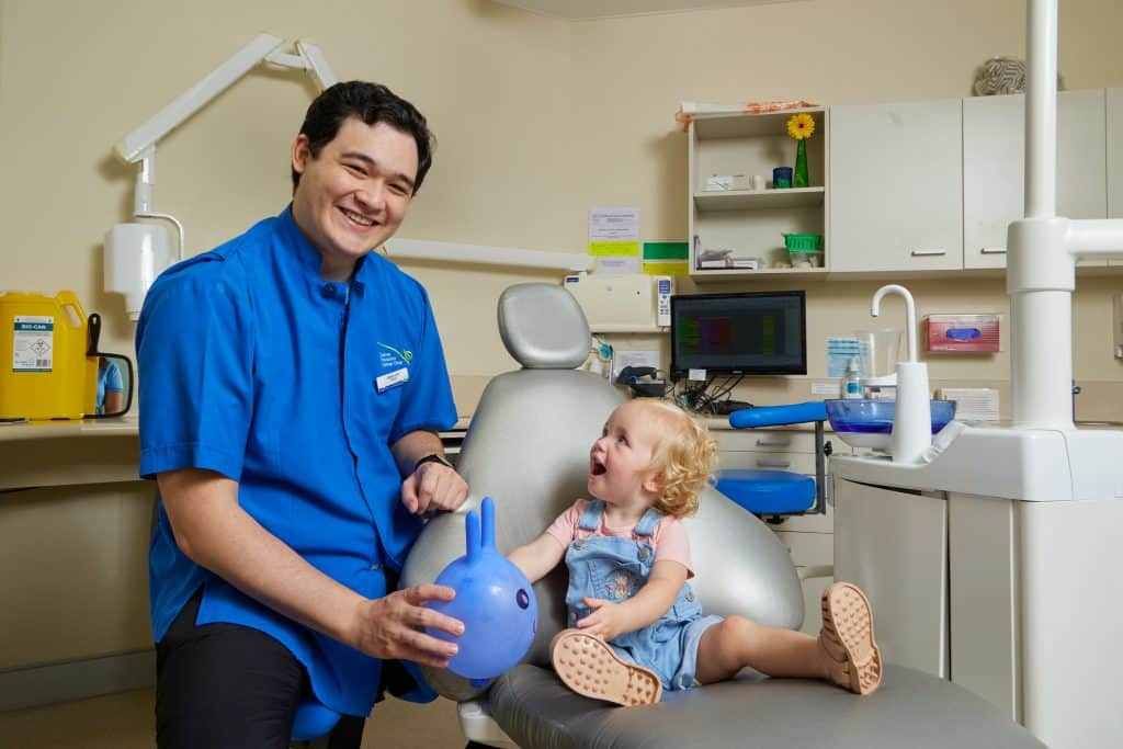 A Dentist is Playing With a Little Girl in a Dental Chair — Cairns Precision Dental Group In Woree, QLD