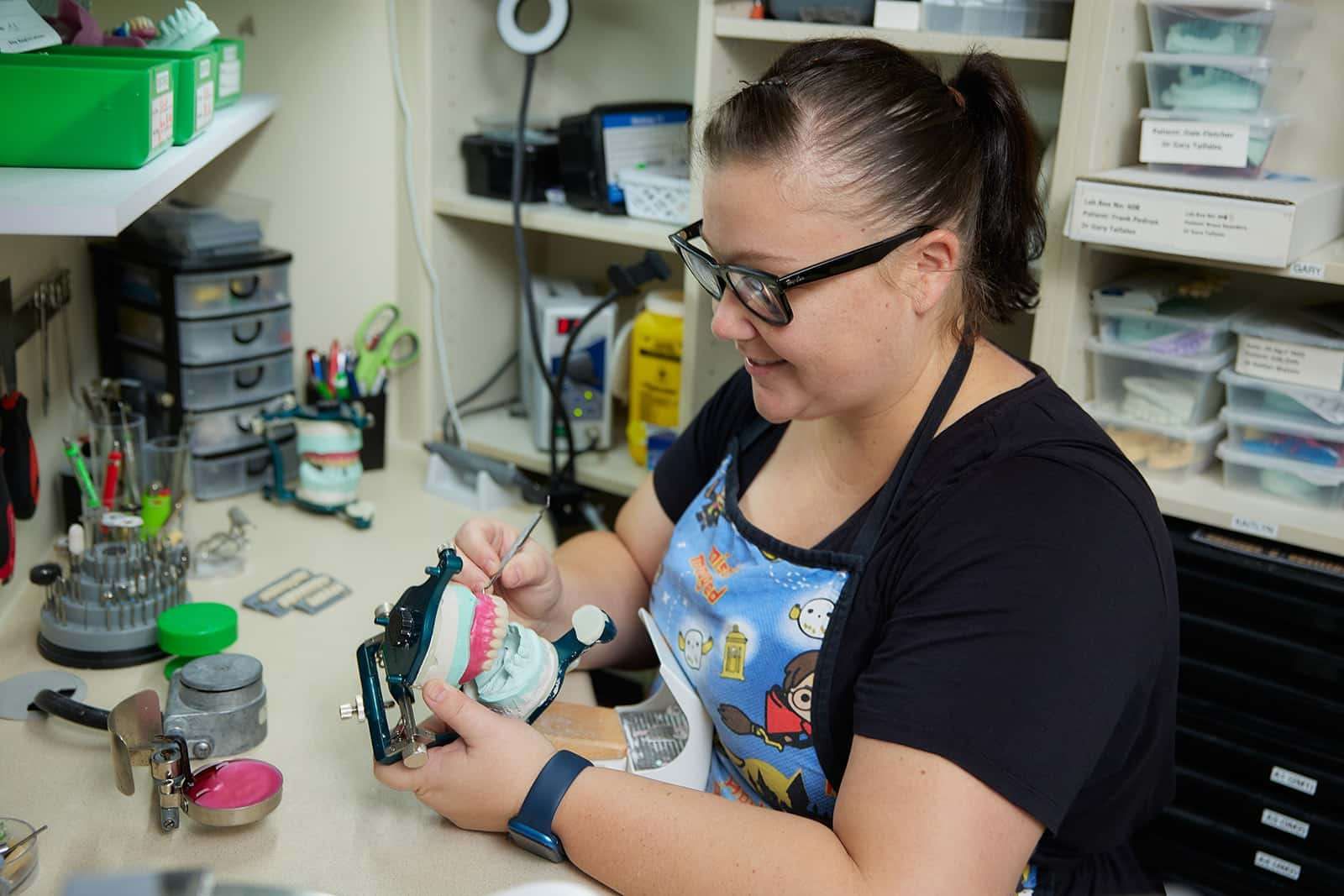 A Woman is Working on a Denture in a Dental Office — Cairns Precision Dental Group In Woree, QLD