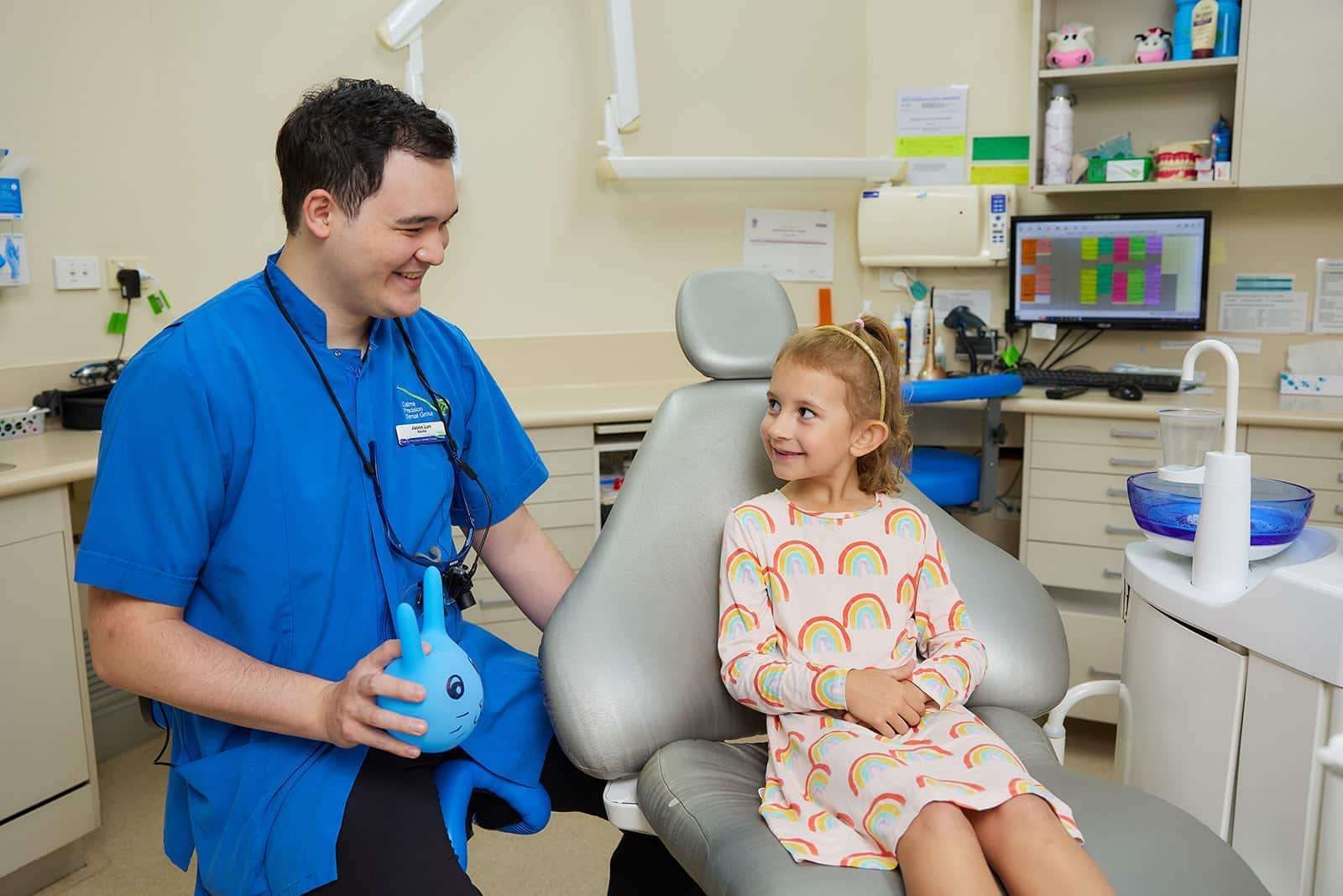 A Little Girl is Sitting in a Dental Chair Talking to a Dentist — Cairns Precision Dental Group In Woree, QLD