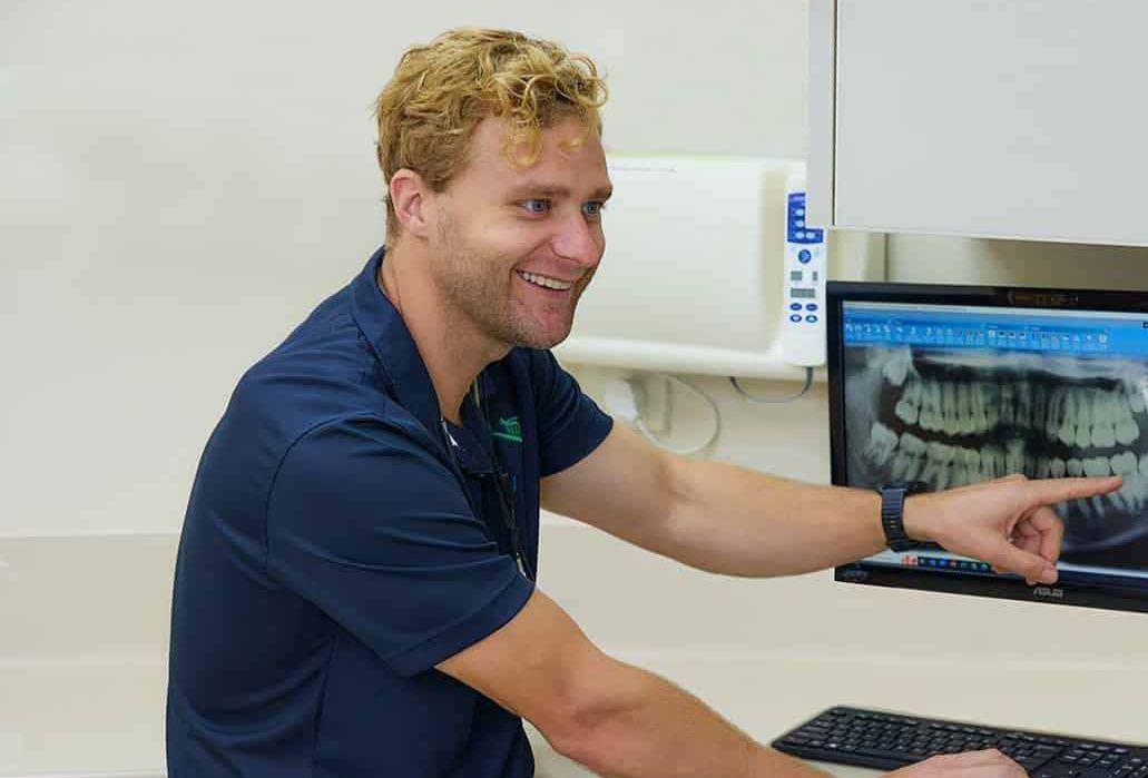 A Man and a Woman Are Sitting at a Desk Looking at a Computer Screen — Cairns Precision Dental Group In Woree, QLD