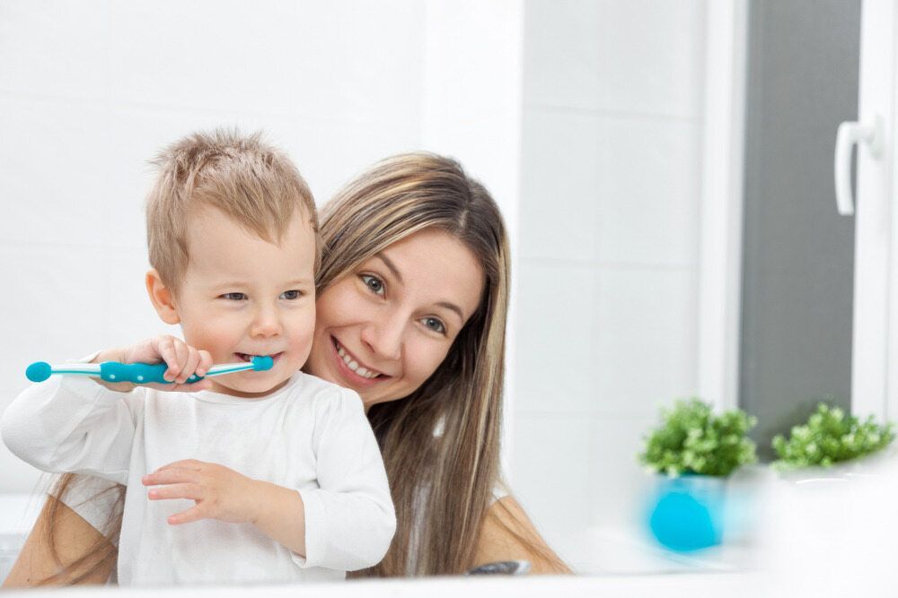 A Woman is Brushing Her Child's Teeth in Front of a Mirror — Cairns Precision Dental Group In Woree, QLD
