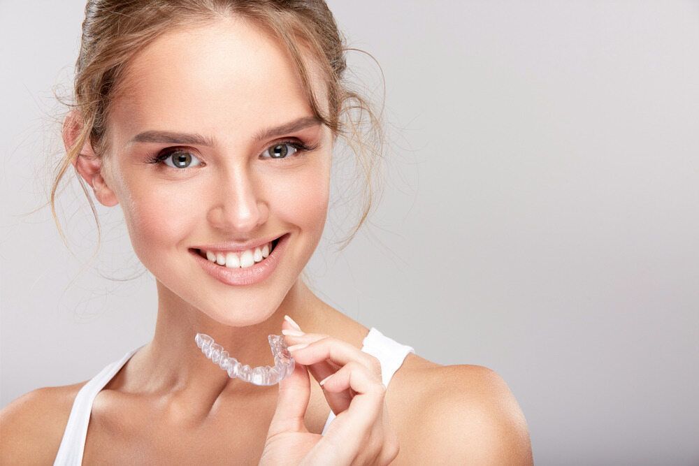 A Woman is Smiling While Holding a Clear Brace on Her Neck — Cairns Precision Dental Group In Woree, QLD