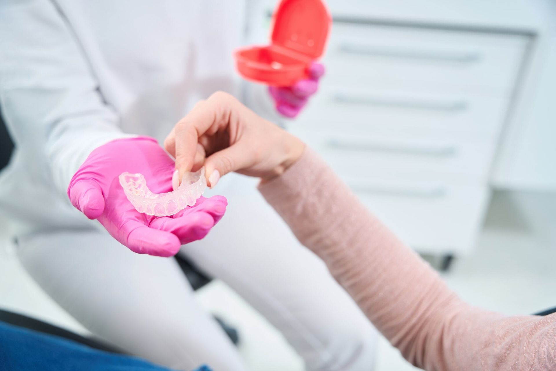 A Woman Wearing Pink Gloves is Holding a Denture in Her Hand — Cairns Precision Dental Group In Woree, QLD