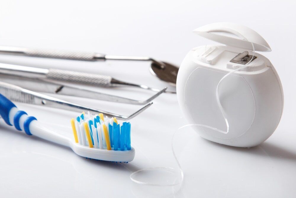 A Toothbrush and Dental Floss Are on a White Surface — Cairns Precision Dental Group In Woree, QLD