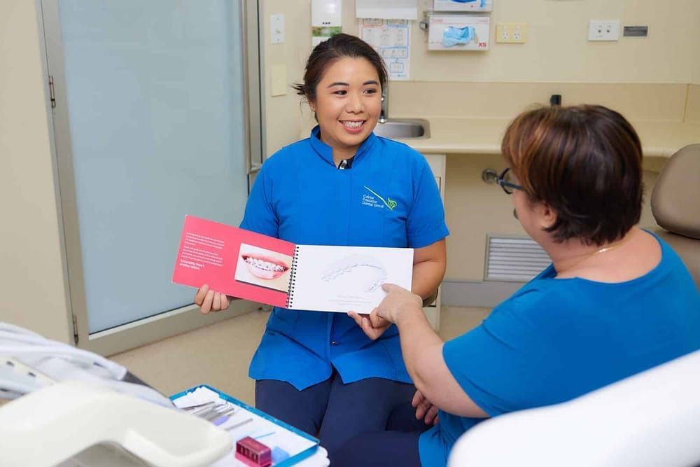 A Woman is Sitting in a Dental Chair Holding a Book  — Cairns Precision Dental Group In Woree, QLD