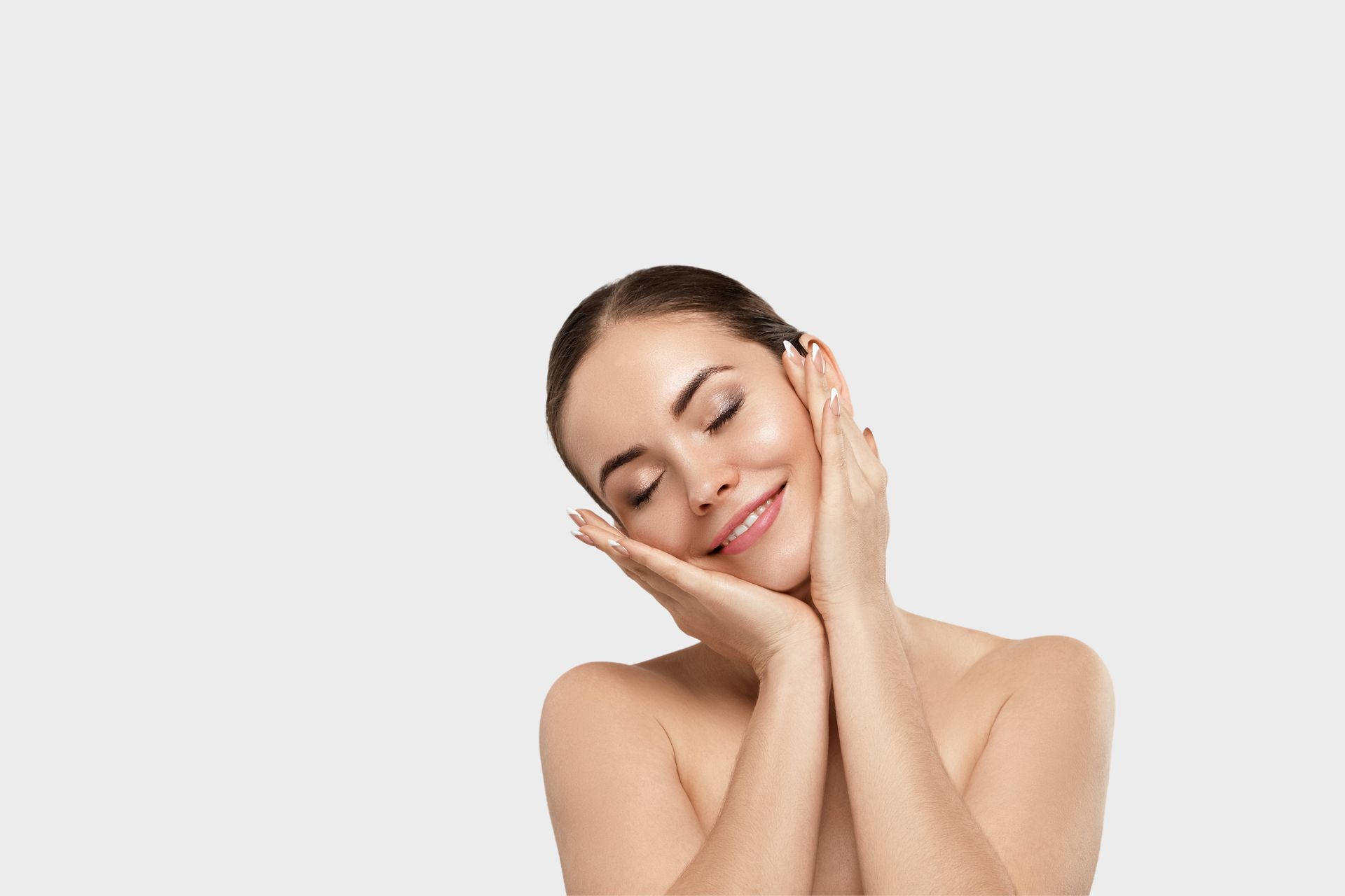 A woman is touching her face with her hands and smiling.