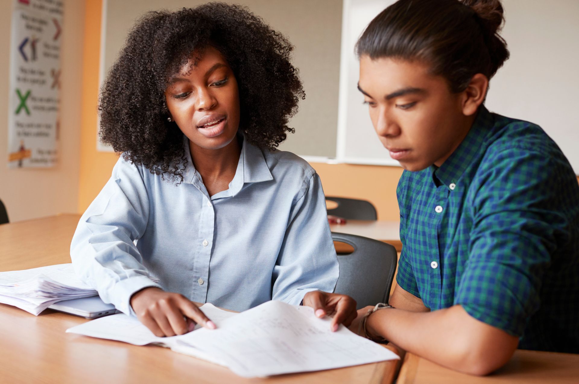 A woman is helping a young man with his homework in a classroom.