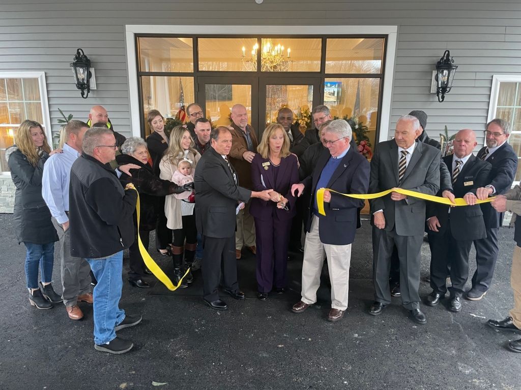 A group of people are cutting a yellow ribbon in front of a building.