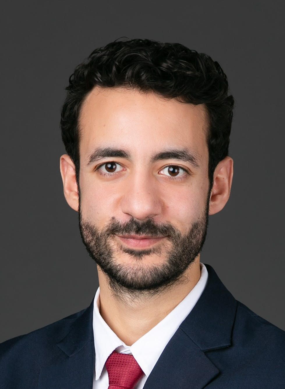 Man with light hair smiles, wearing a light blue button-down shirt. White background.