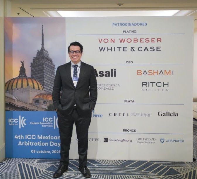 Man in a suit stands in front of a green backdrop with 