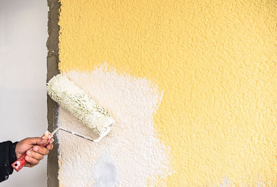 Painter rolling white paint on a yellow wall. Learn about Dallas Painting Solutions' expert residential painting services.