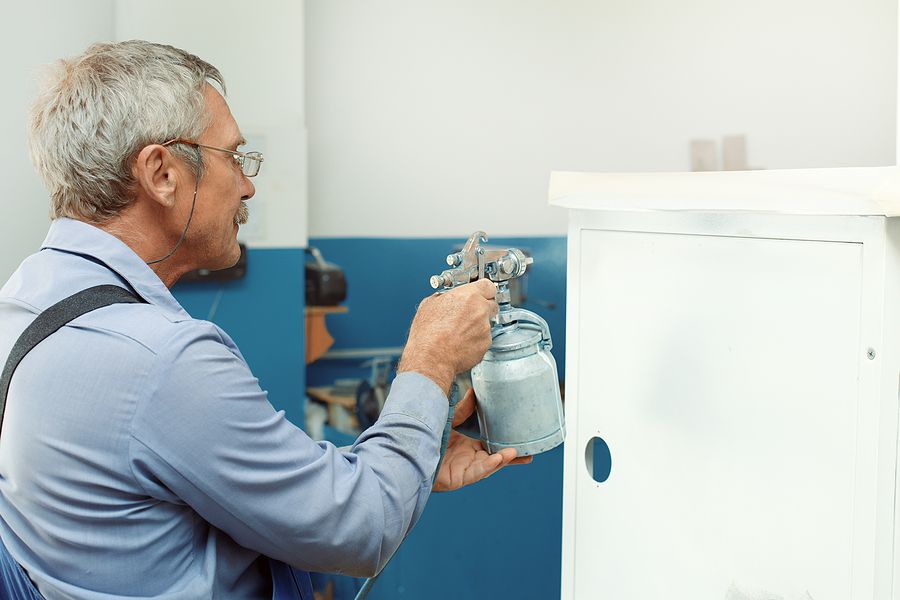 Older man painting a cabinet with a brush. Professional cabinet refinishing in Dallas for a fresh, modern look.