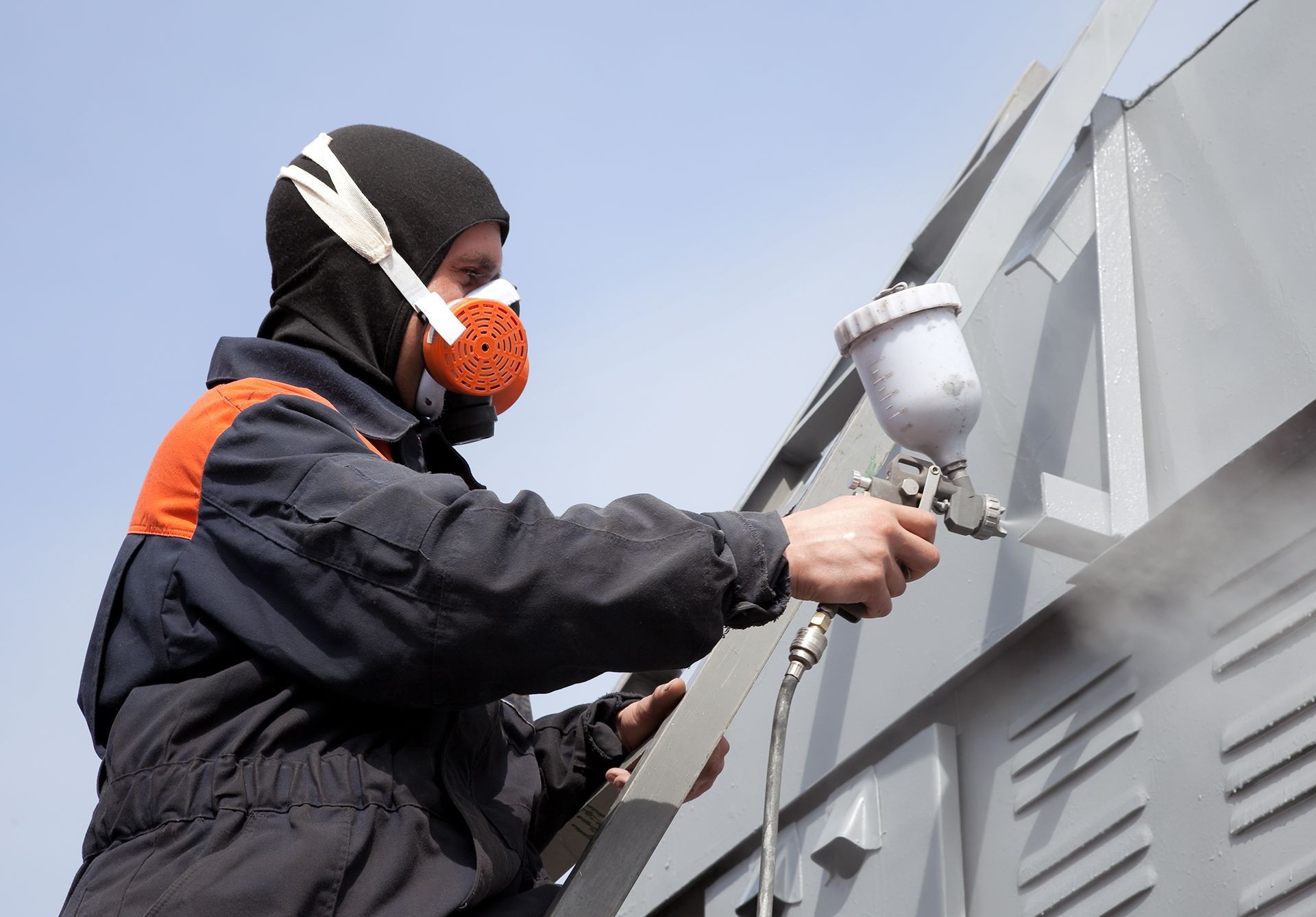 A professional painter wearing protective gear is spraying paint on a commercial building exterior. Expert commercial painting services in Dallas