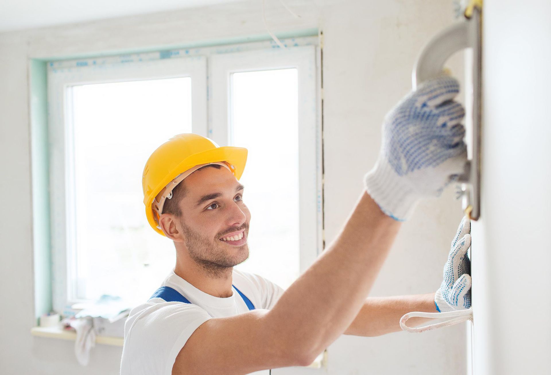 Worker in a hard hat repairing drywall with a trowel. Get quick and professional drywall repair services in Dallas.