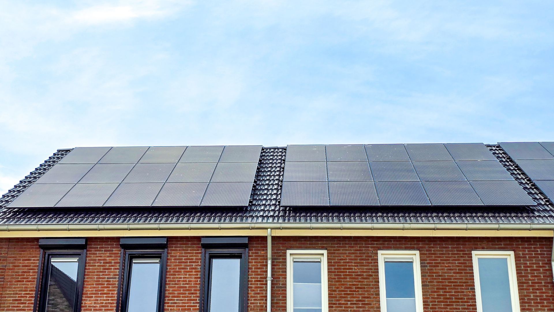 Een rij bakstenen huizen met zonnepanelen op de daken en een blauwe lucht.